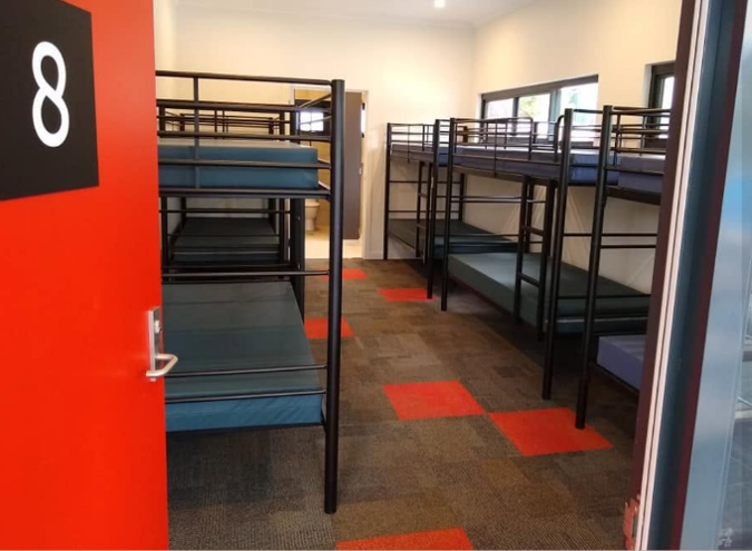 Dormitory room with metal bunk beds in two rows, blue mattresses, and an orange door labeled 8.